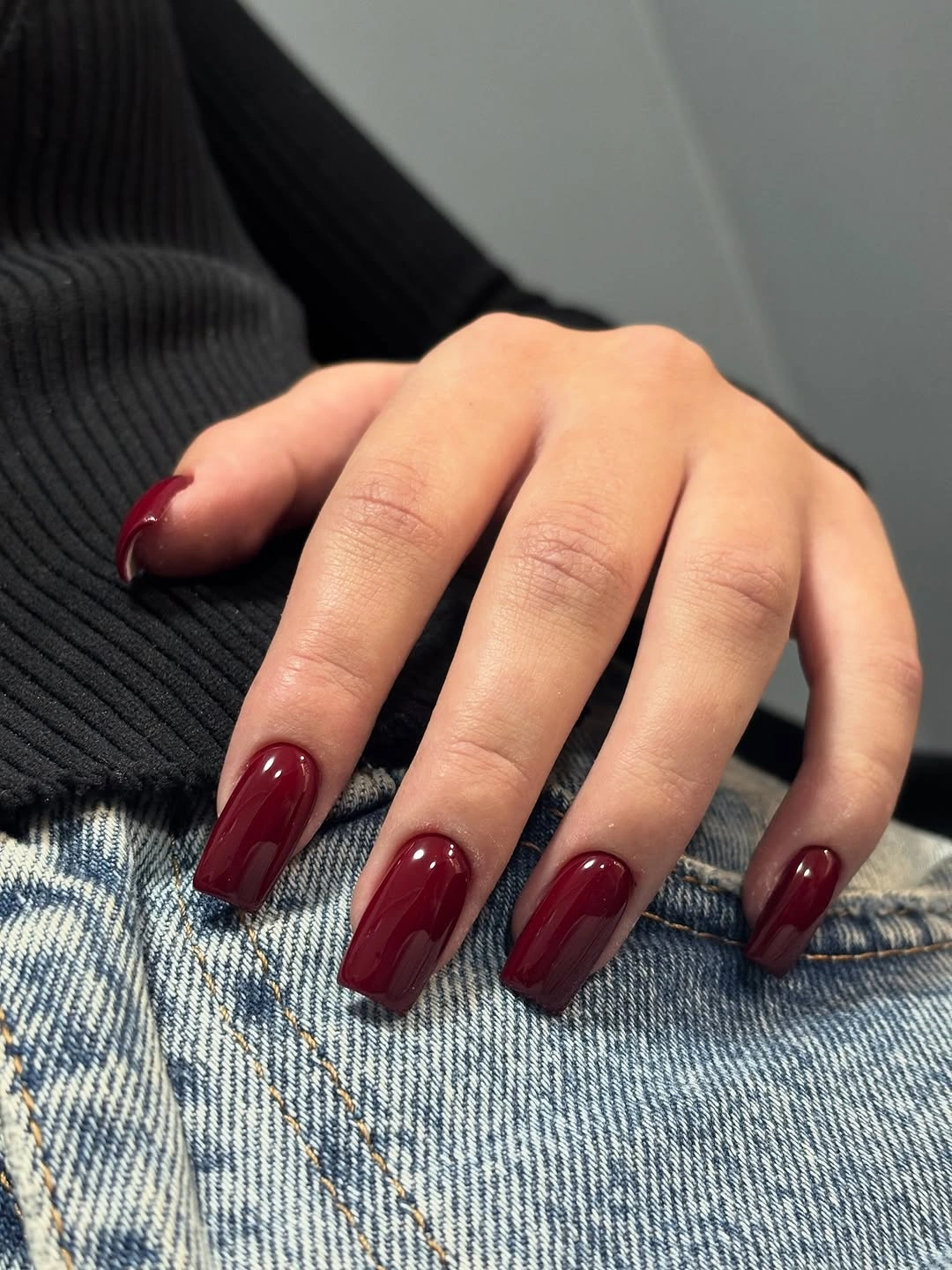 wine burgundy square nails resting against blue denim