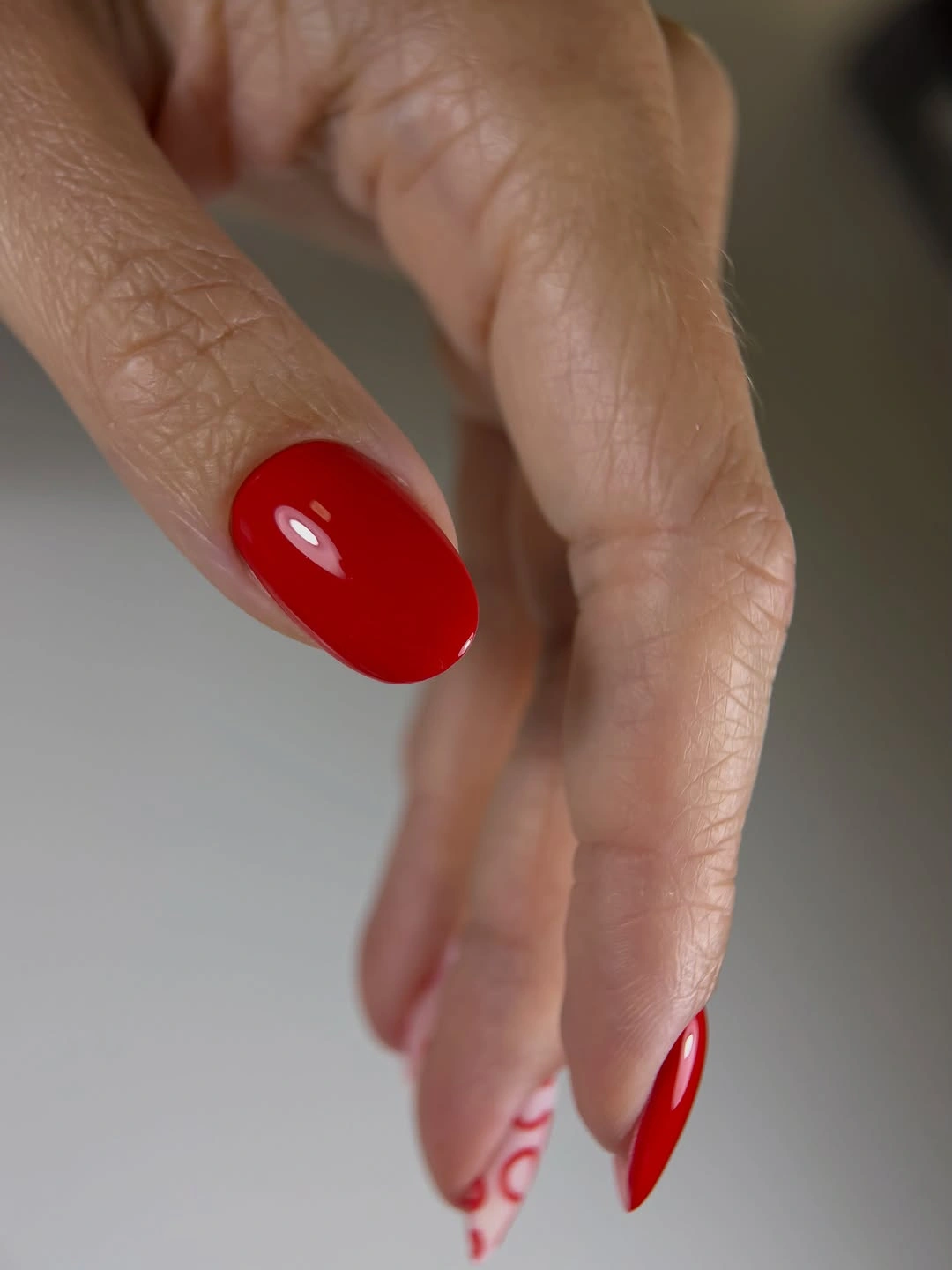Glossy red almond nails with red swirl accent