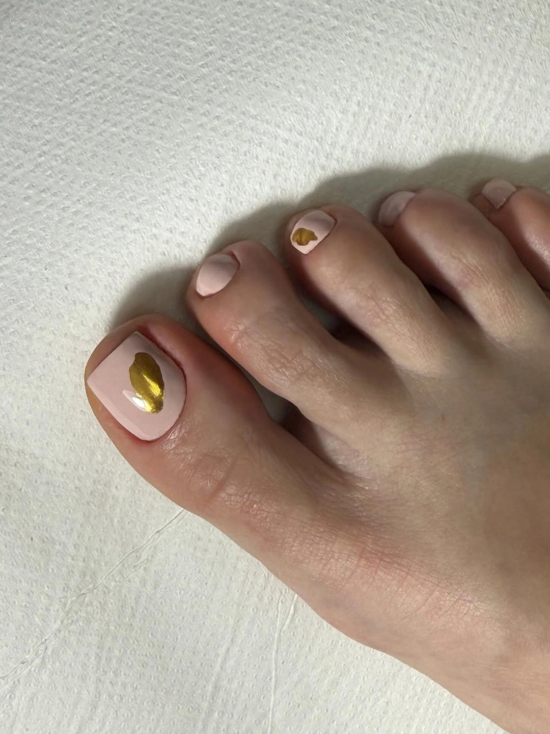 nude pink pedicure with metallic gold accents