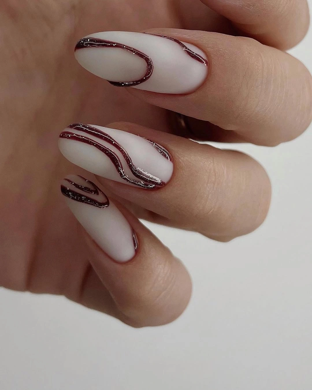 Long milky almond nails with thin burgundy curved lines
