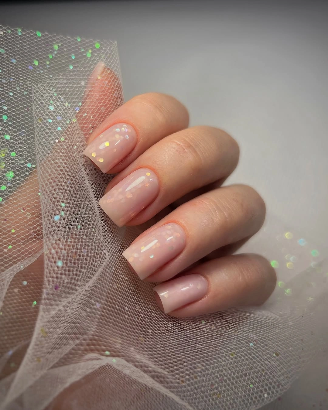 Short blush nails with sparse pastel confetti accents