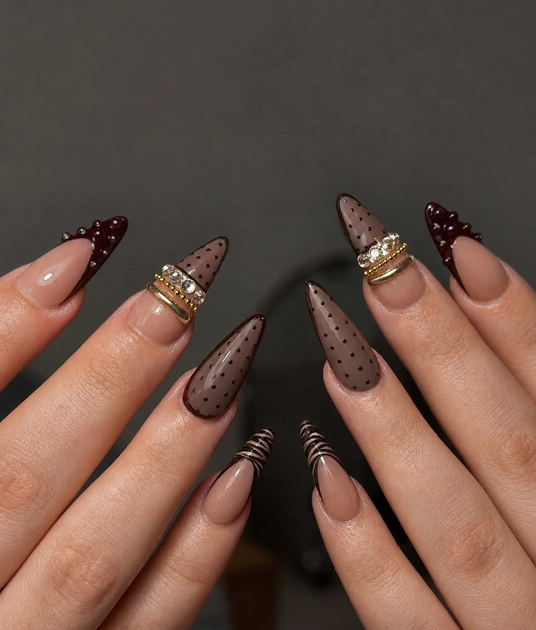Long almond burgundy nails with black panels and warm ornamental accents