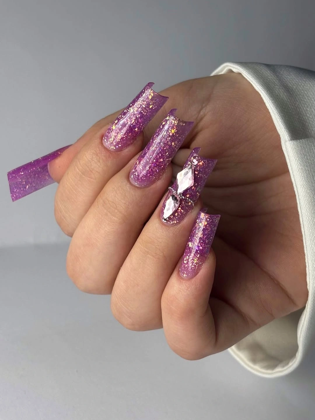 Long square magenta glitter nails with one large reflective bow accent