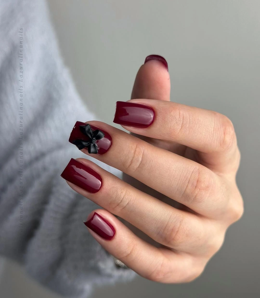 Square burgundy nails with one small bow-like accent