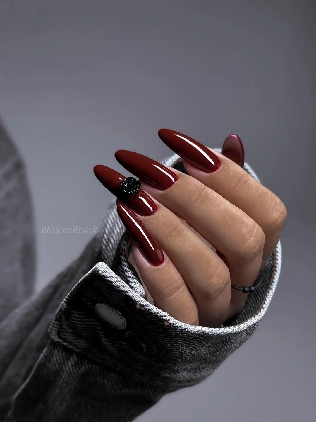 Pointed burgundy stiletto nails with a dark flower accent