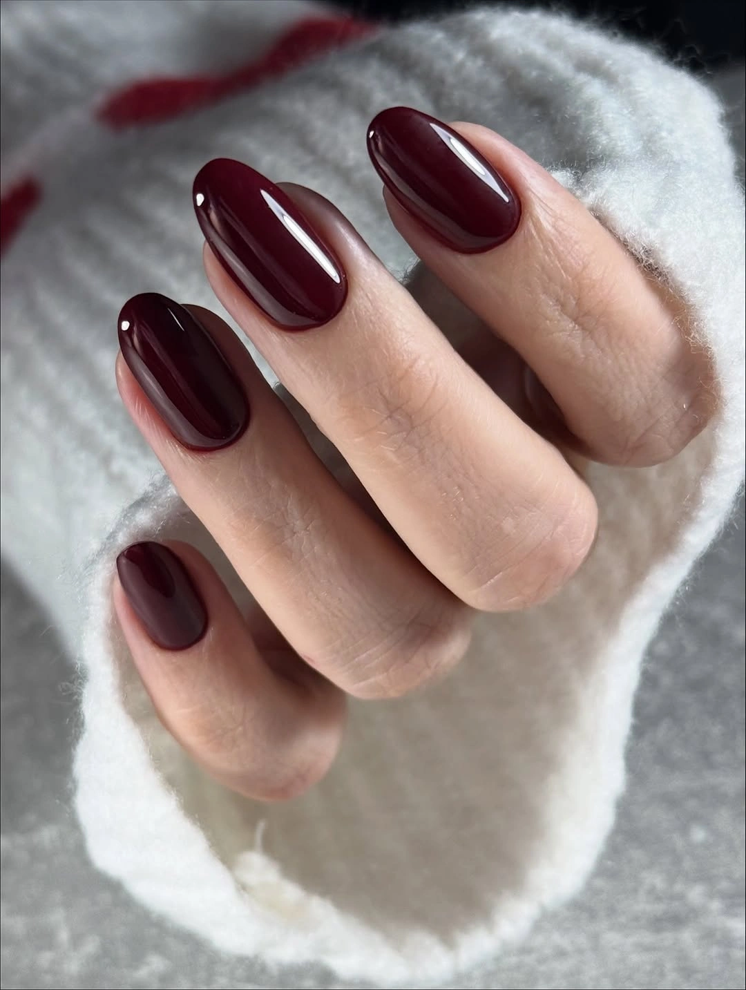 Glossy burgundy oval nails against a pale sweater