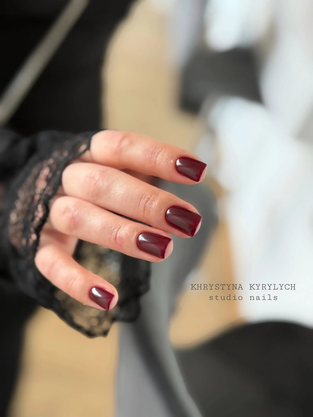 Glossy burgundy rounded-square nails beside gray fabric and black lace