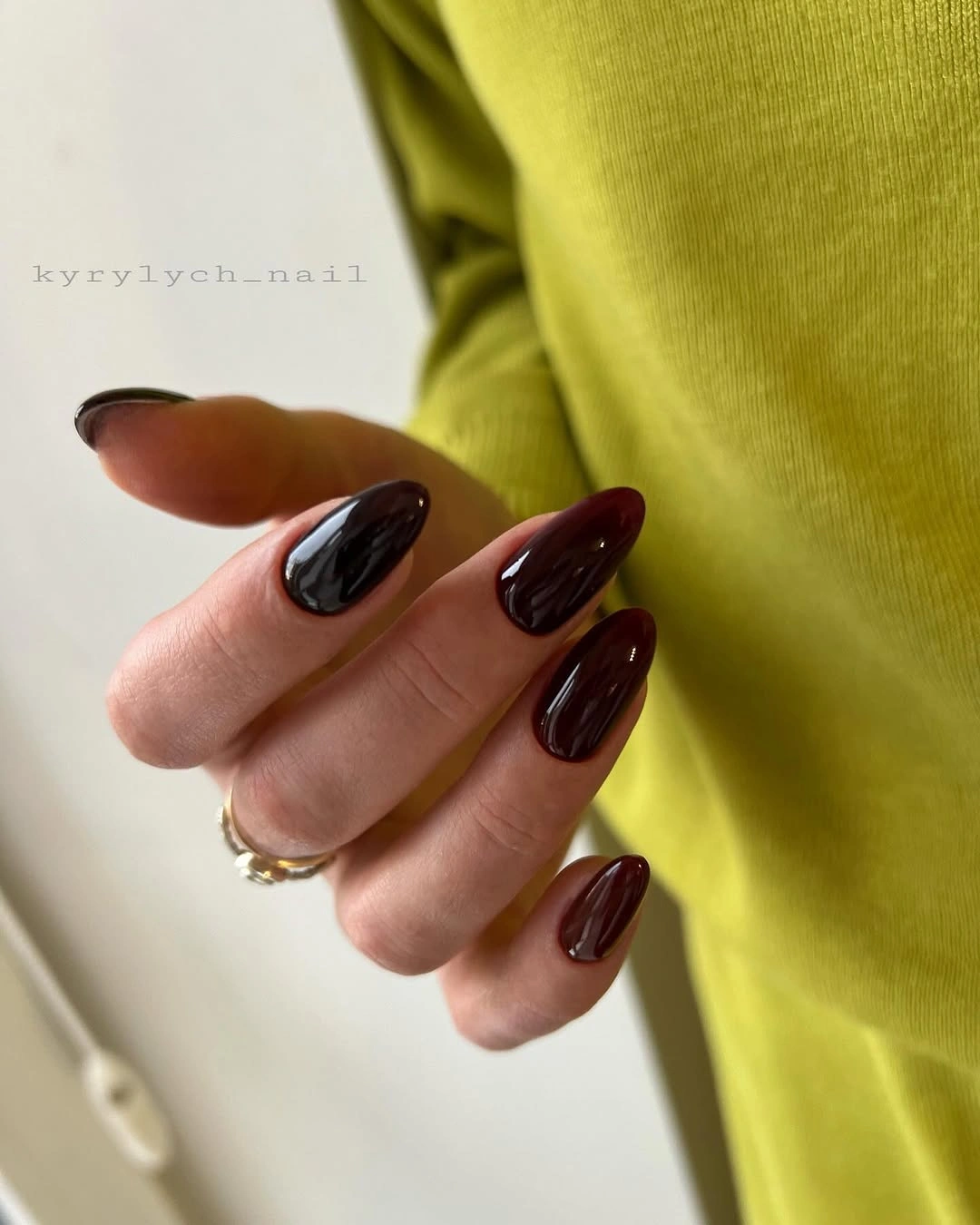 Long glossy dark brown almond nails beside a bright lime knit sleeve