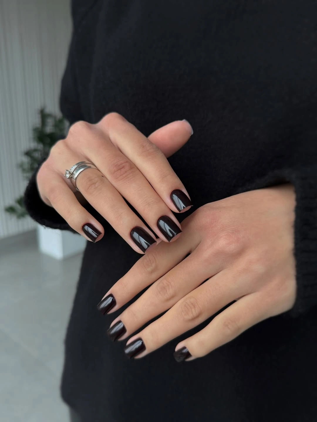 Short dark nails with subtle warm reflective edges and black clothing
