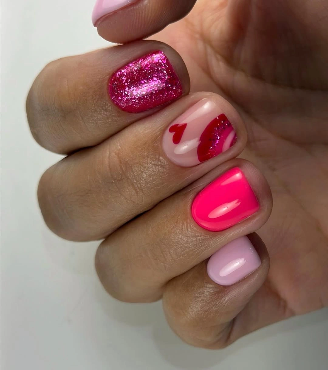 Short bright pink nails with tiny red heart accents