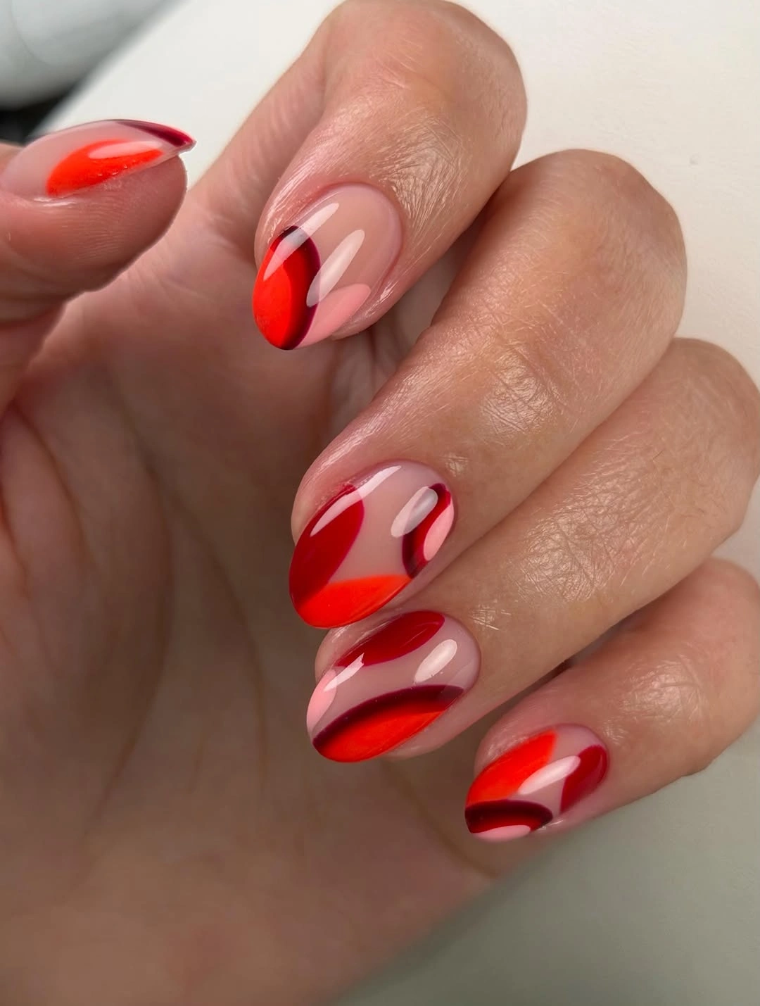 Long almond nails with red arcs over a sheer pink base