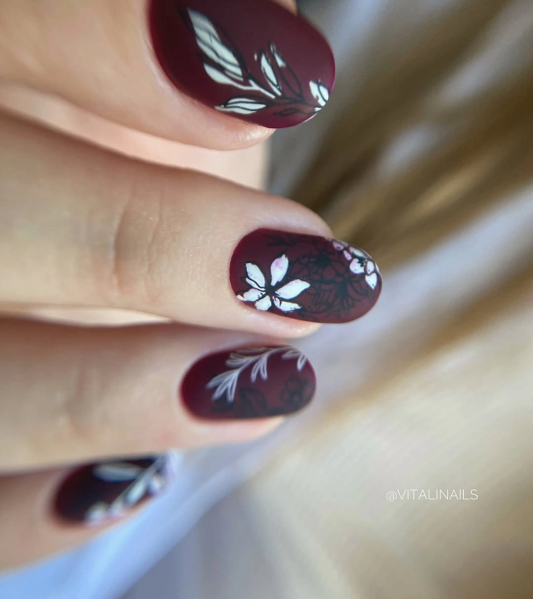 Medium burgundy oval nails with white botanical outlines