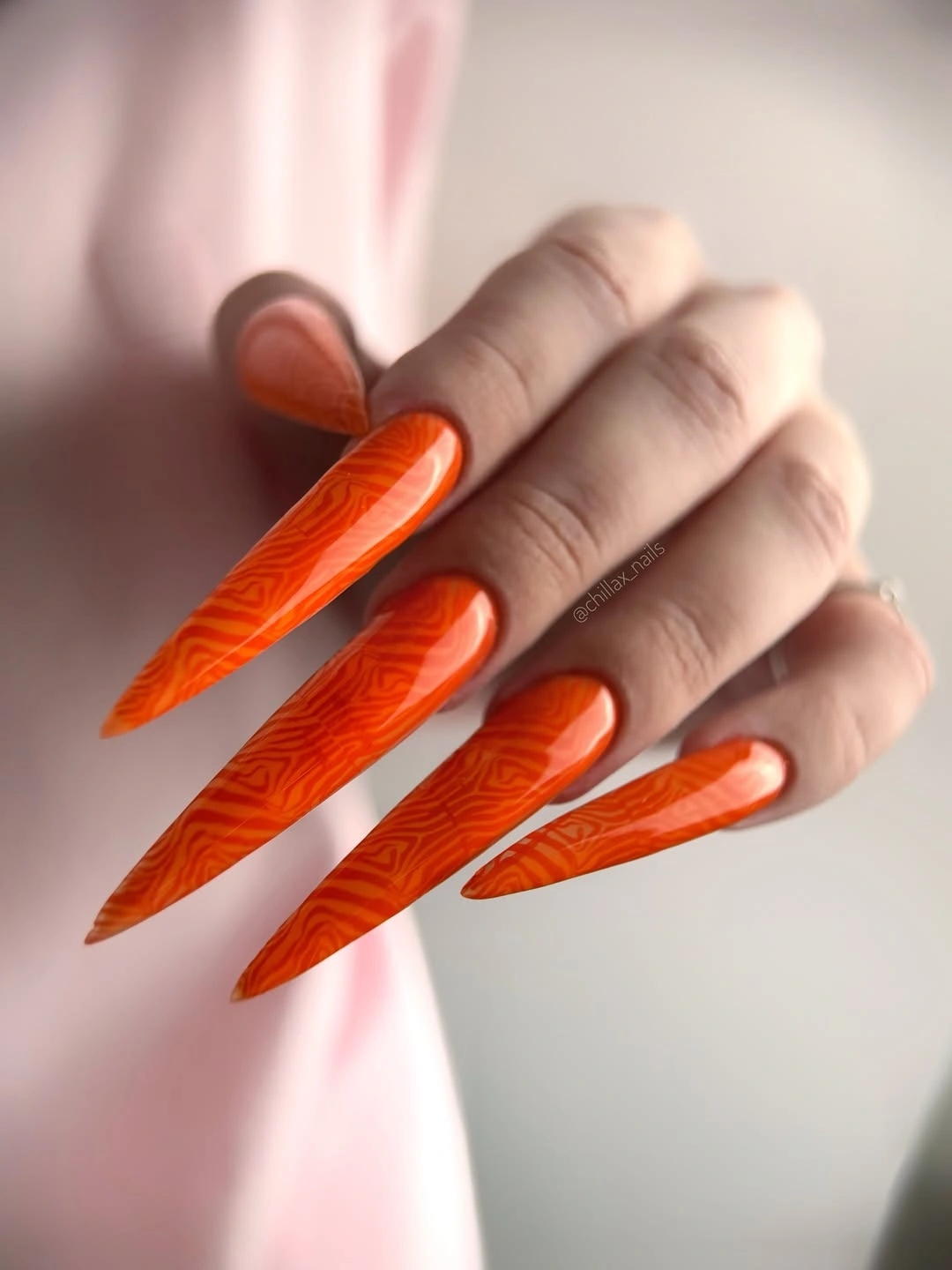 Long orange stiletto nails with darker orange wavy linework