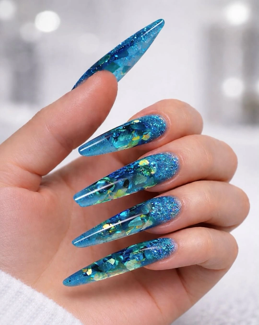 Long blue glitter stiletto nails with aqua depth and warm flecks