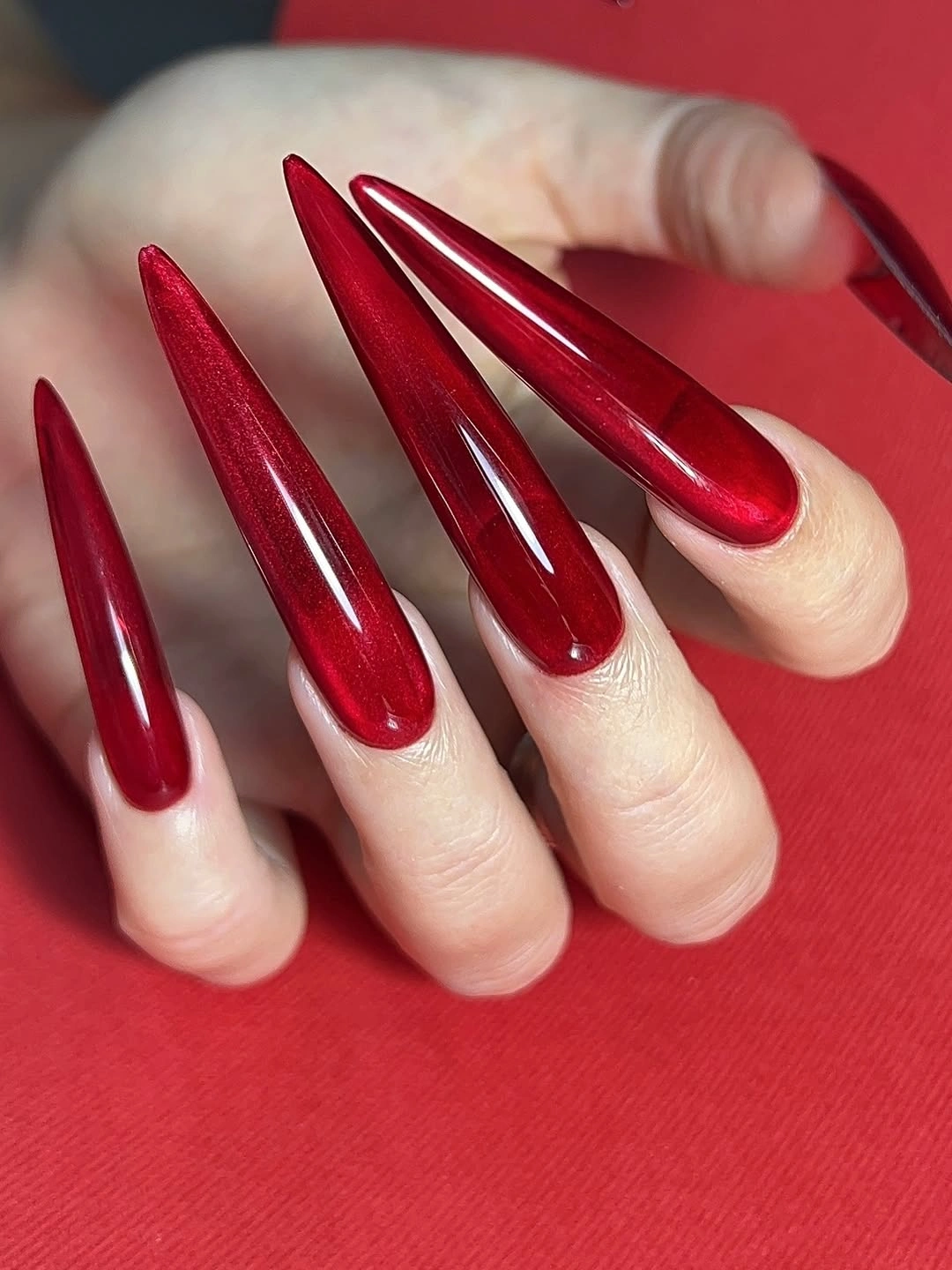 Very long ruby red stiletto nails with a glossy solid finish