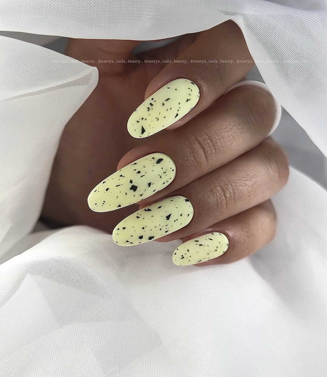 Soft pale-yellow oval nails with small black speckles