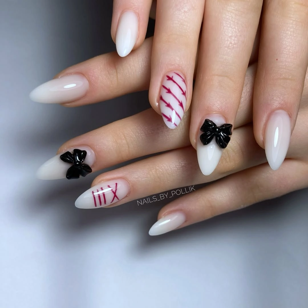 Milky almond nails with small black bow-like and red graphic accents