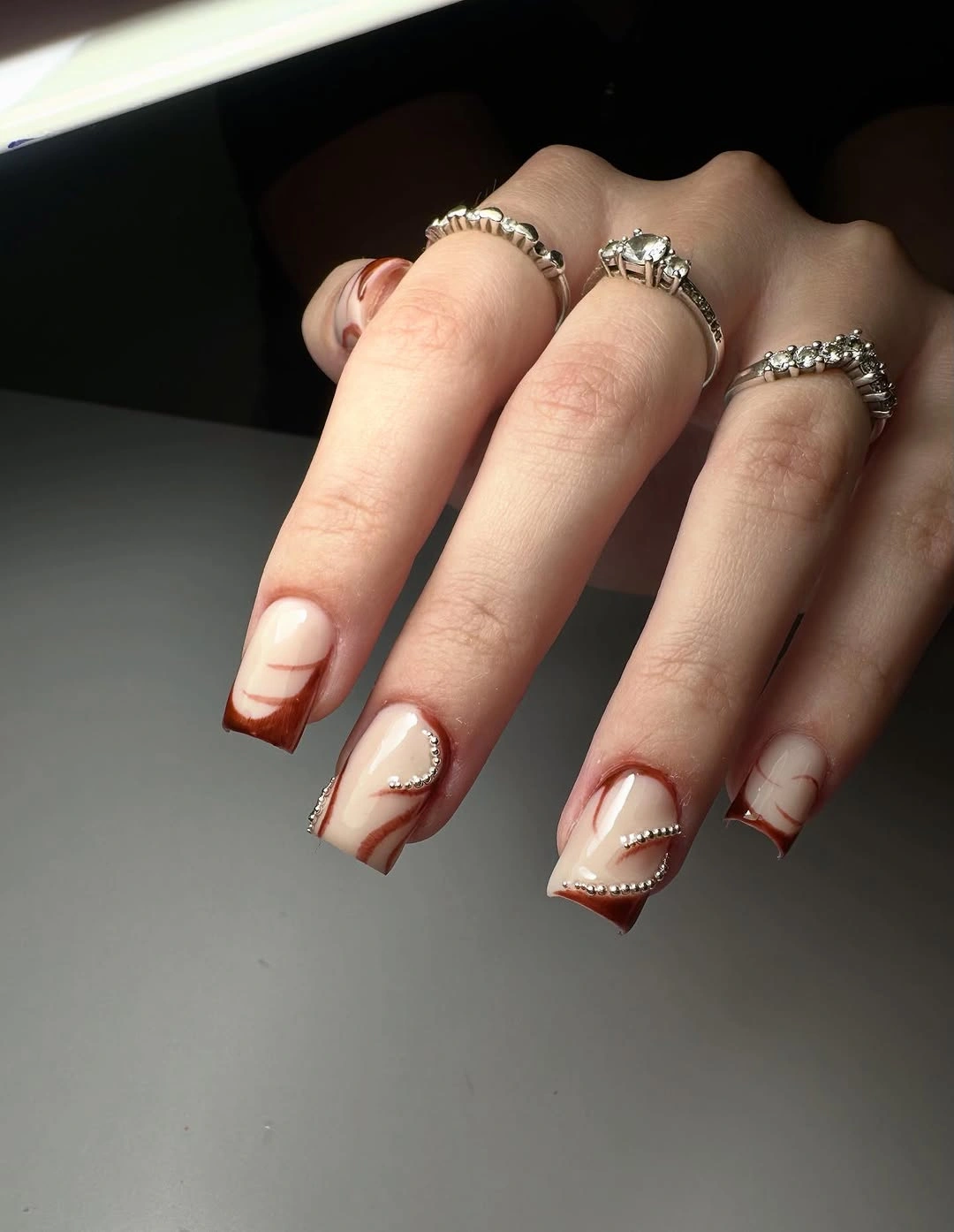 nude square nails with brown curves and silver dots