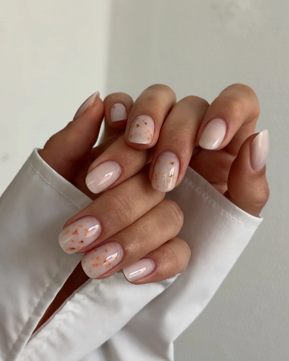 Medium almond nails with a pale nude base and scattered pink coral and green details