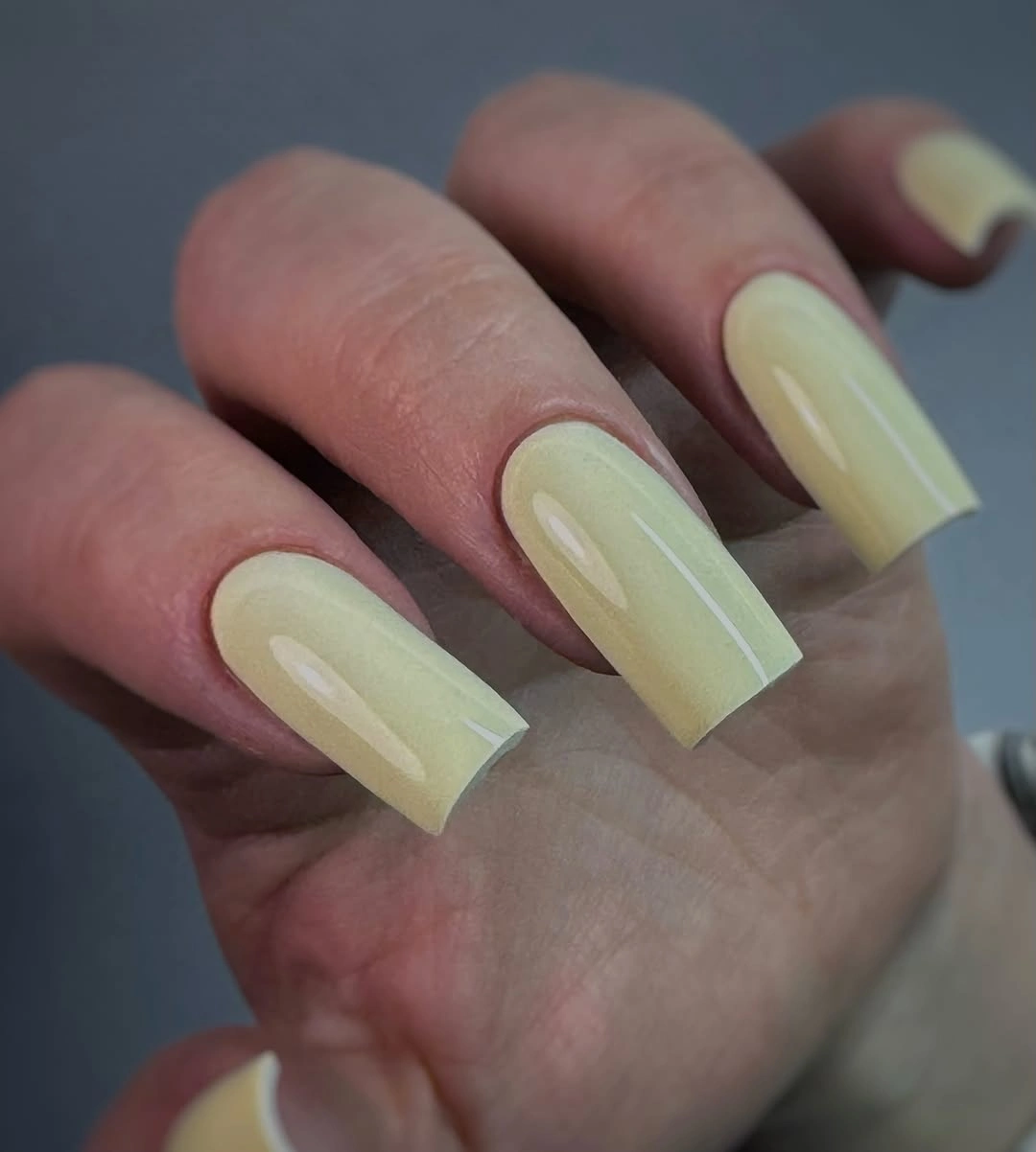 Long square nails in a glossy pale yellow-green cream