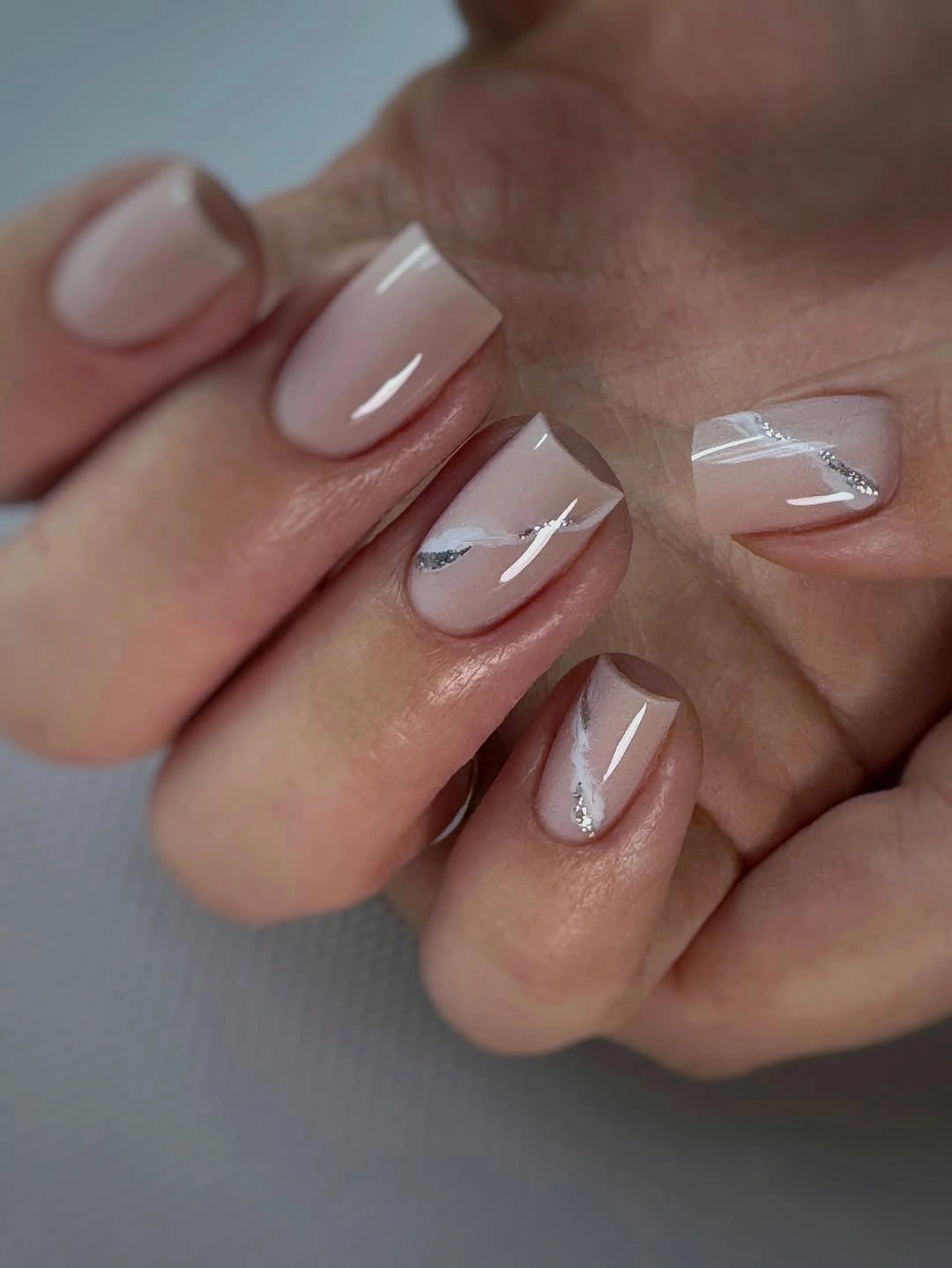 Short almond nails with sheer nude pink bases and white and silver diagonal accents