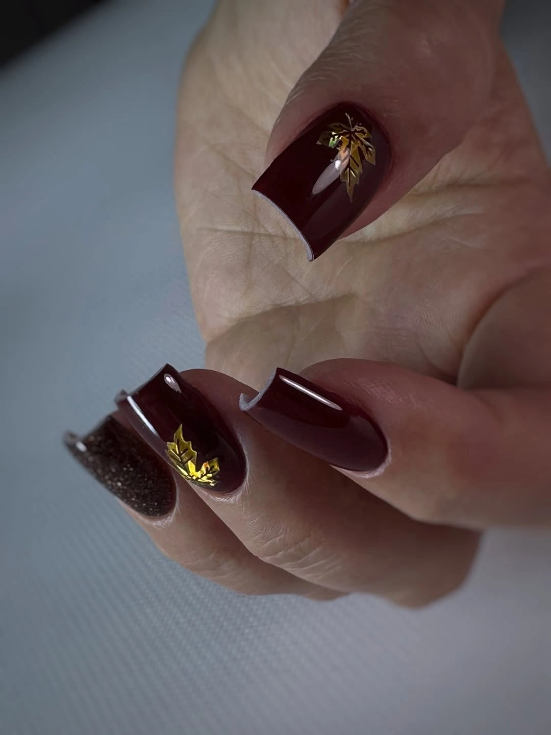 Medium square nails in brown red with a dark accent glitter nail and tiny gold detail