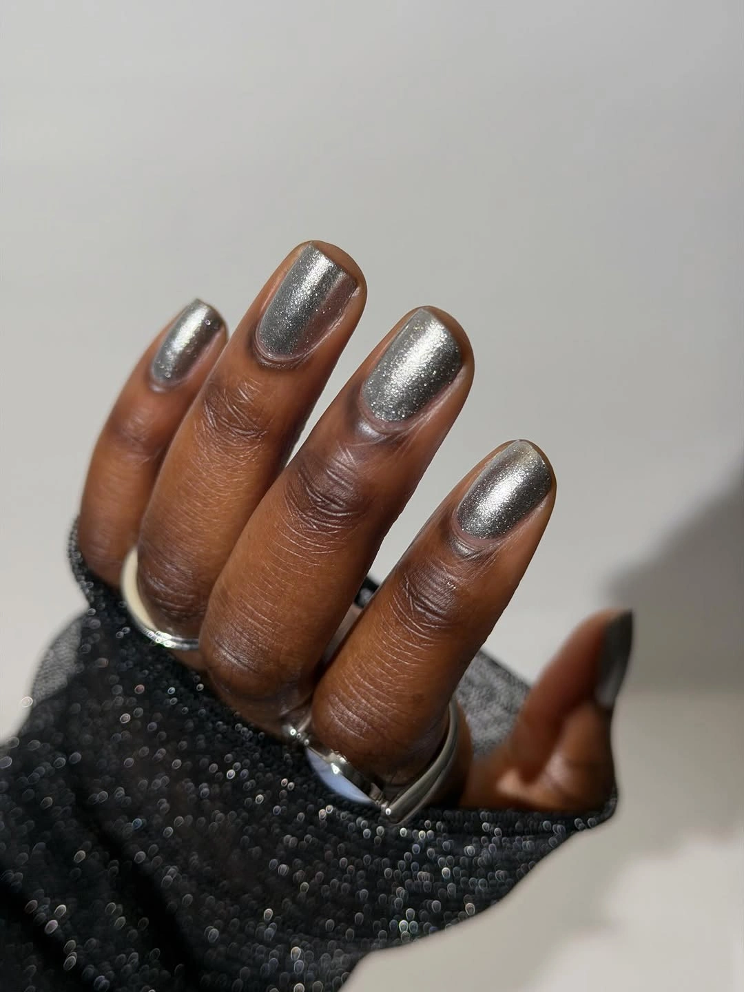 Short silver metallic rounded square nails against dark fabric