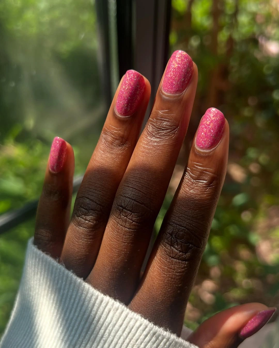 Short hot pink nails with fine shimmer in outdoor light