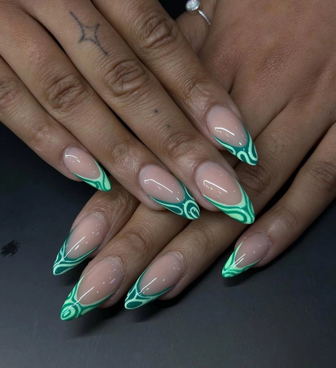 Nude almond nails with emerald green tips and curved lines