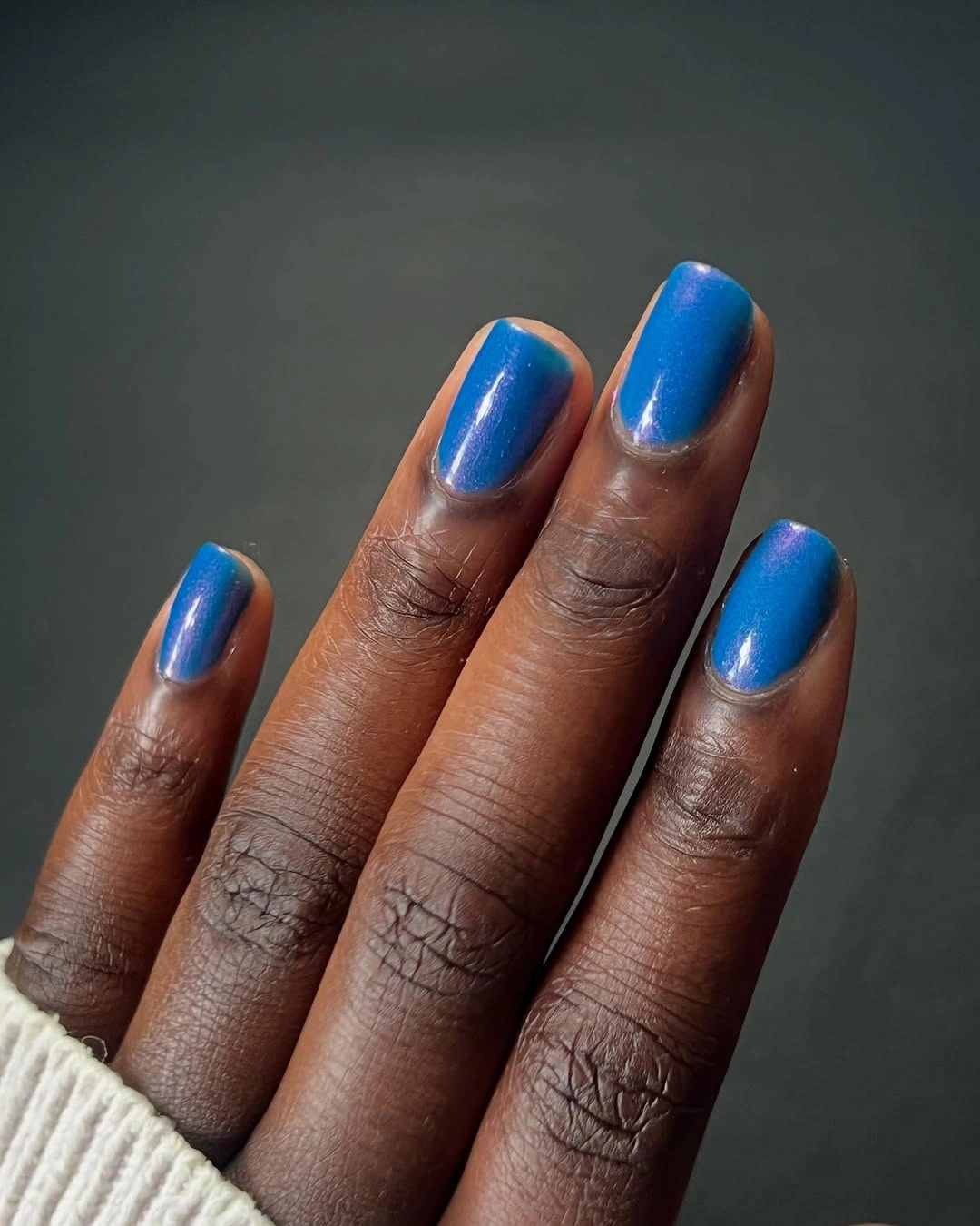 Short cobalt blue metallic square nails against dark fabric