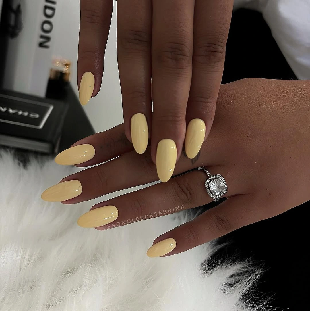 Long glossy pale yellow almond nails with a clean finish