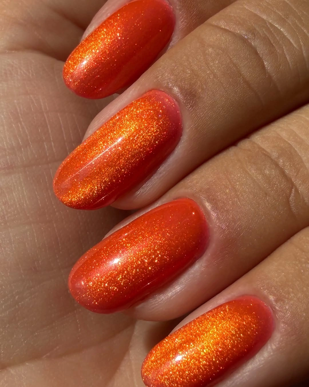 Medium oval orange red nails with fine reflective shimmer