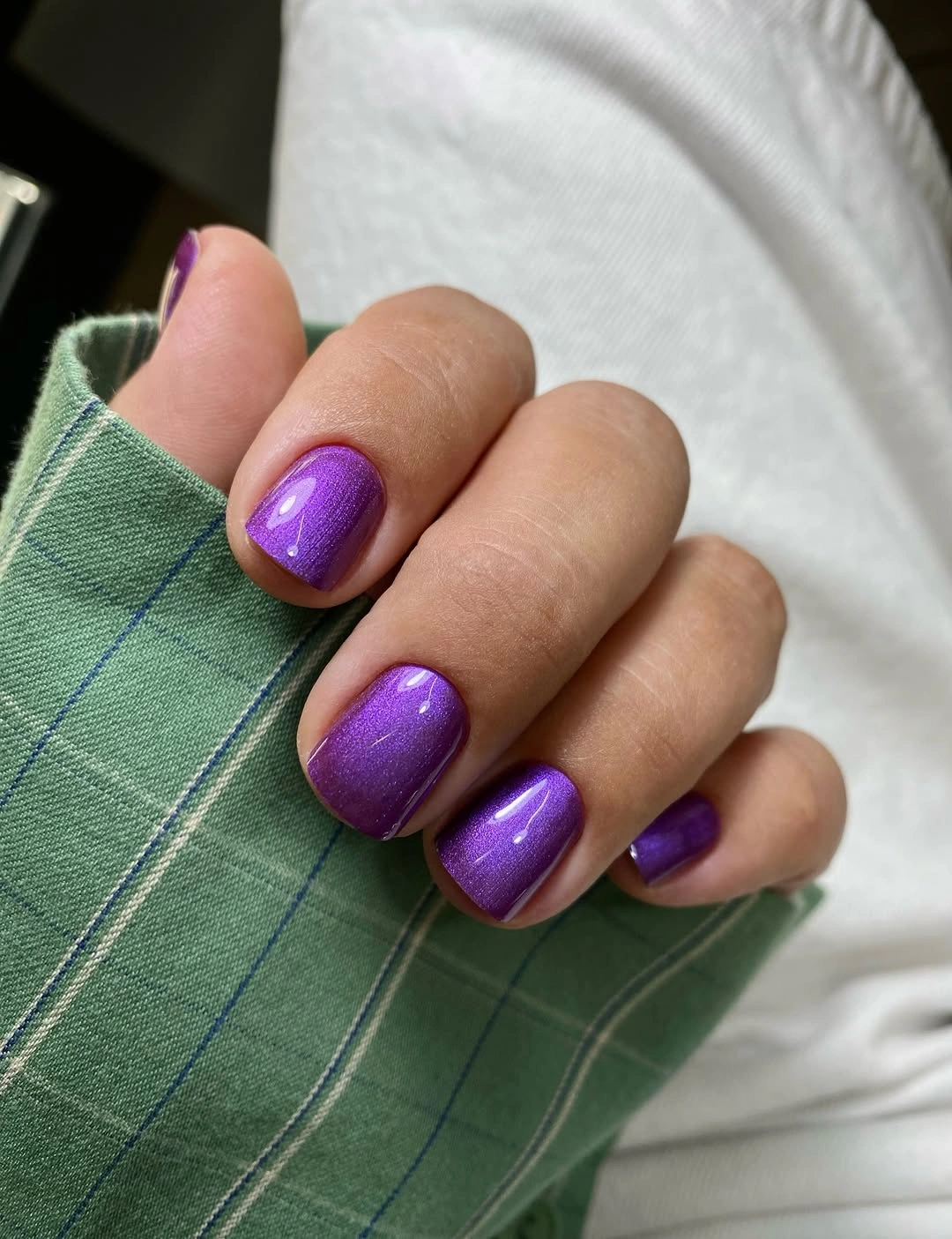 Short purple rounded-square nails beside a green sleeve