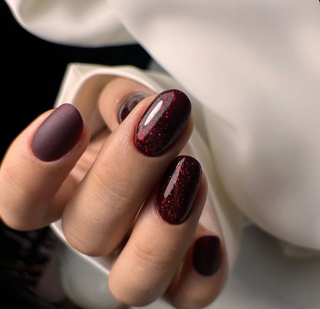 Short plum burgundy nails with one red sparkle accent