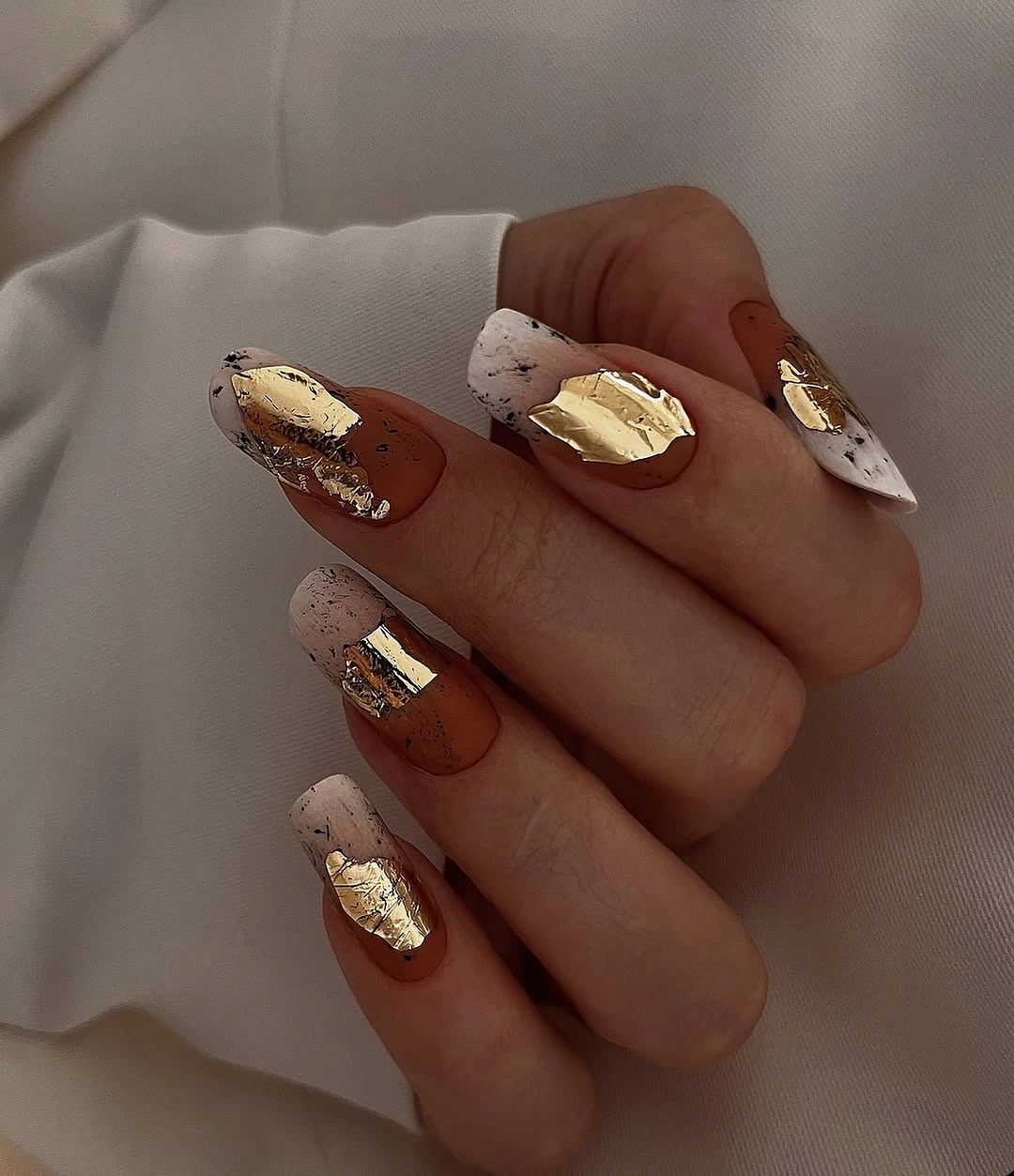 Long warm brown almond nails with speckled and gold accents