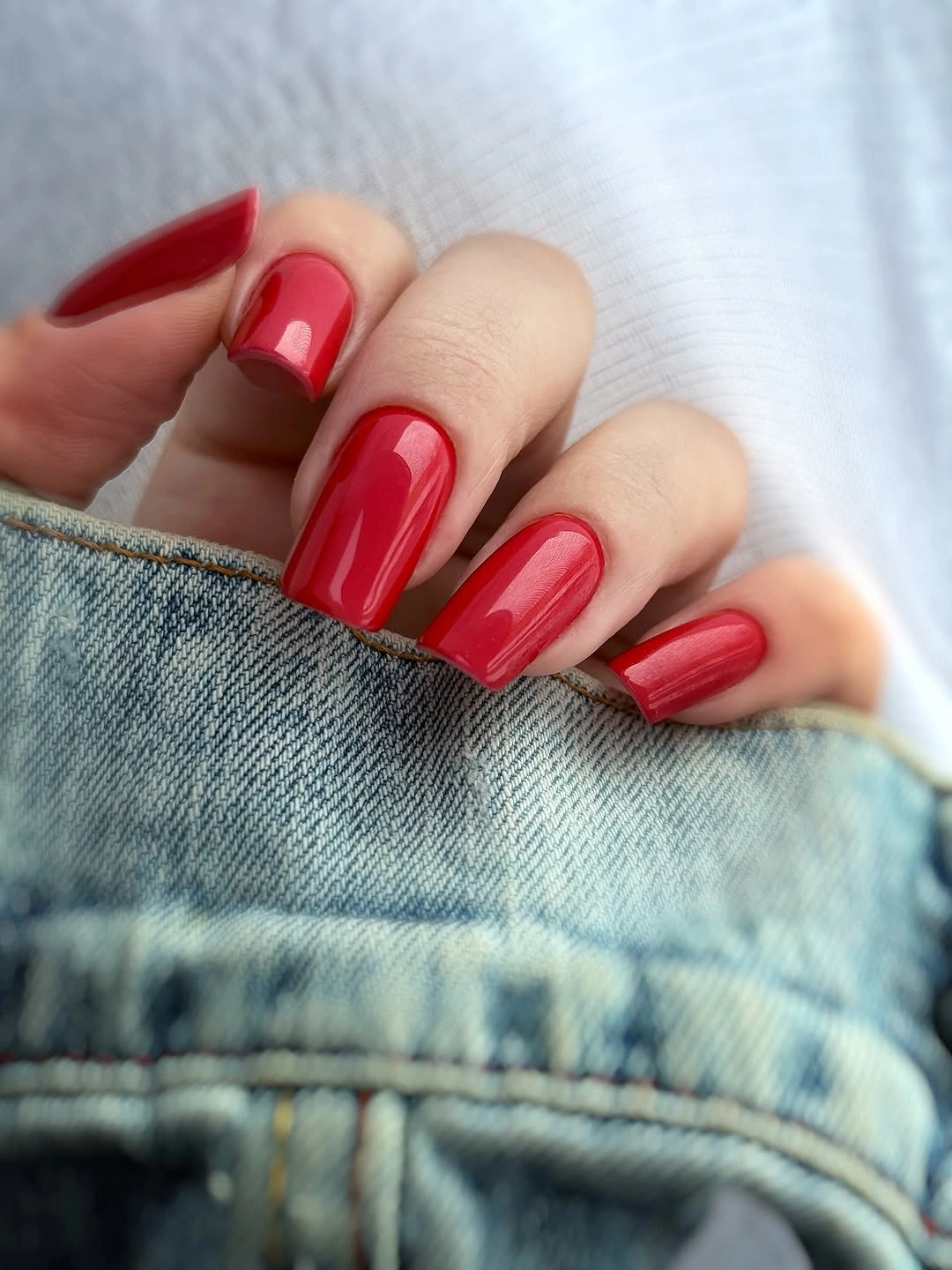 Short glossy bright red nails against light denim