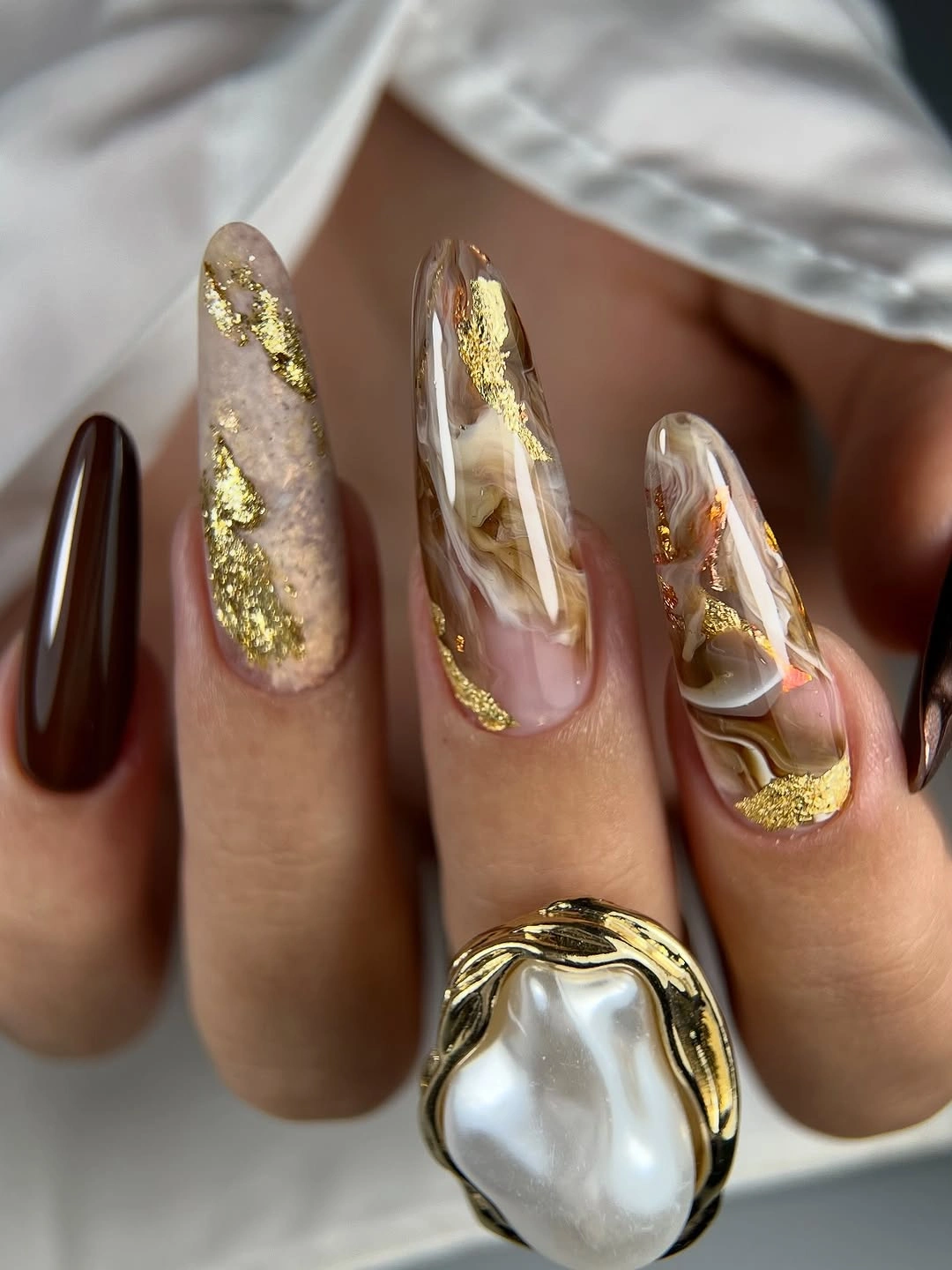 Long almond nude nails with irregular gold and pale marbled accents
