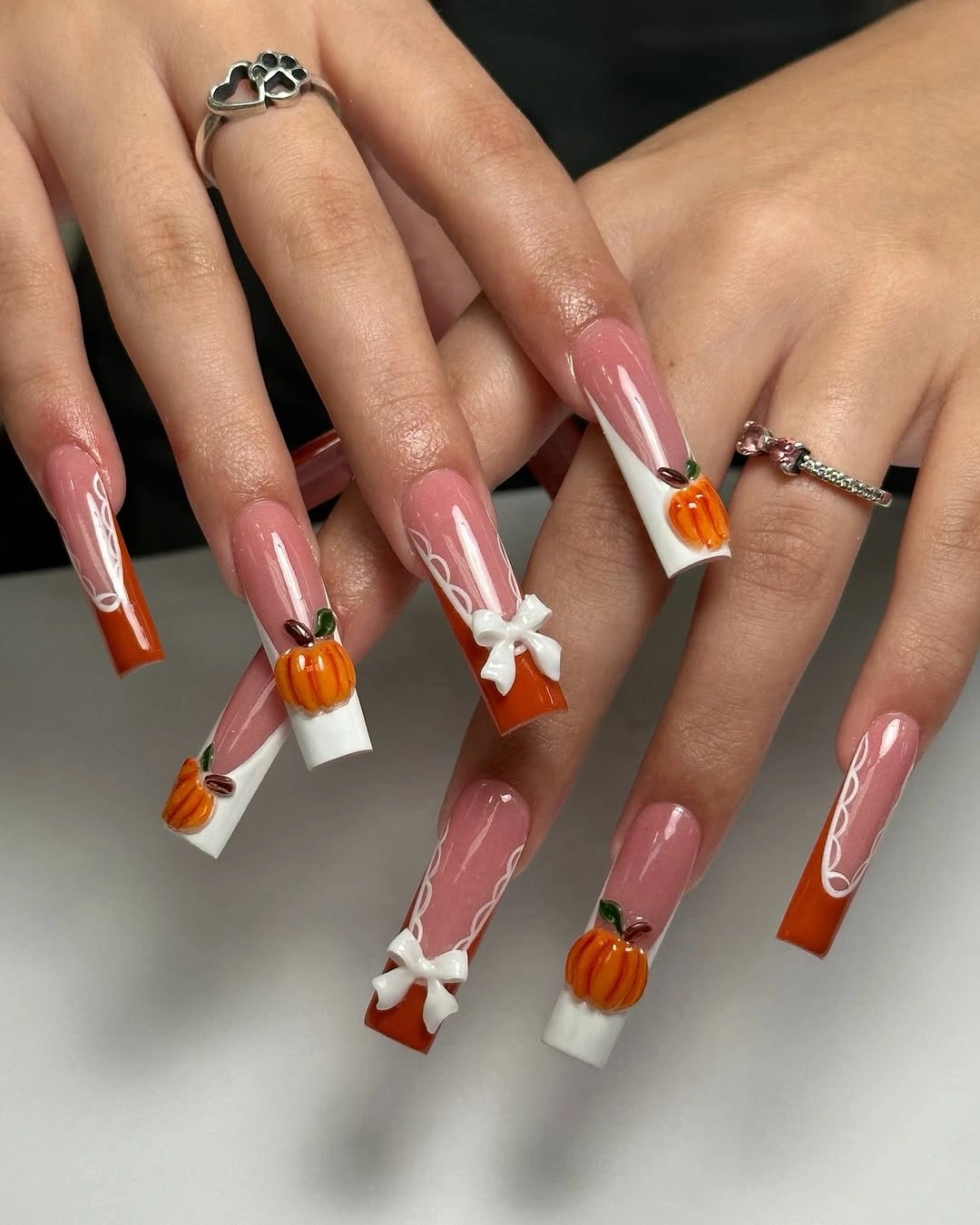 Long coffin nude nails with orange pumpkin tips and white bows