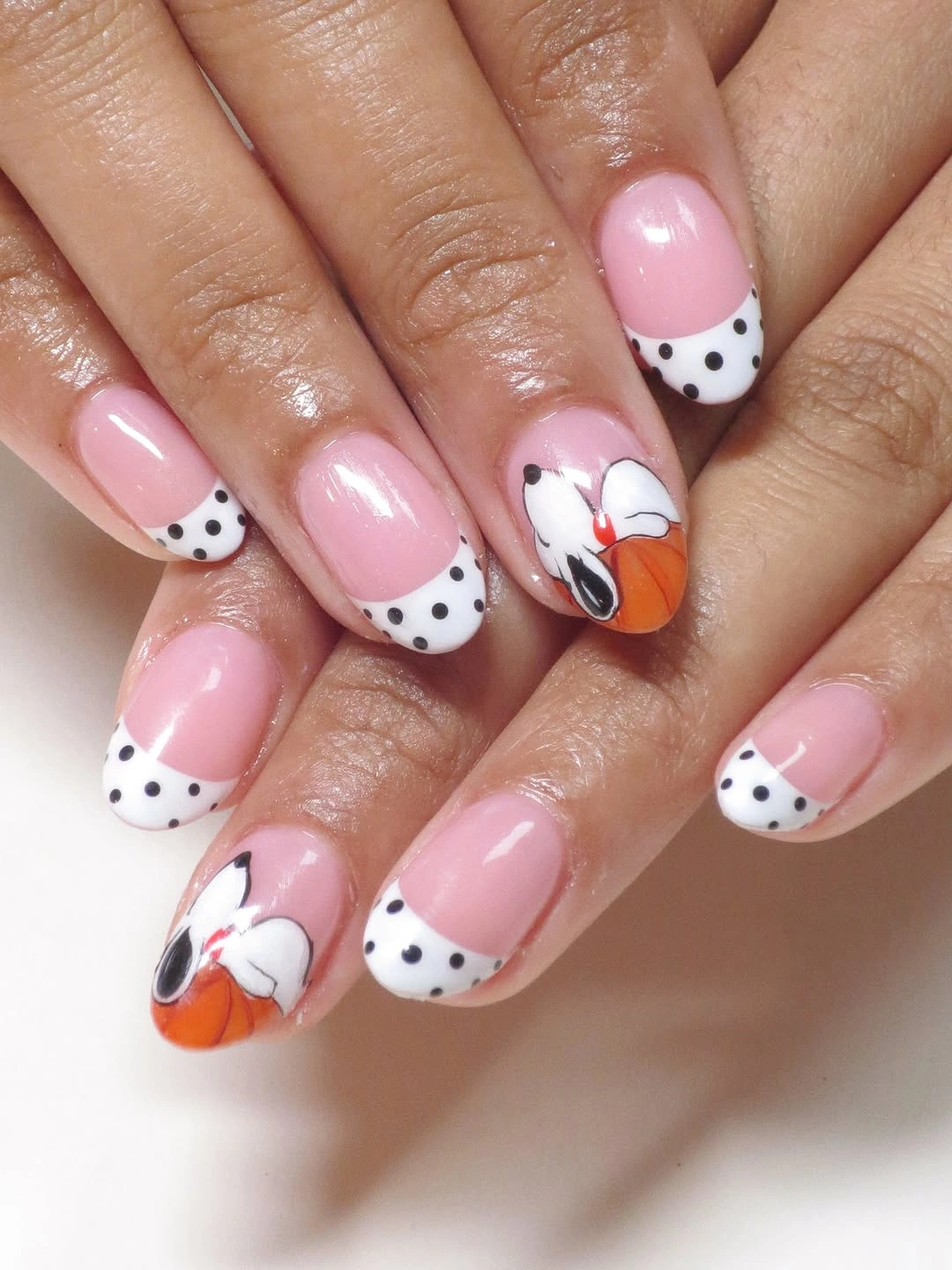 Short almond pink nails with dotted white tips and pumpkin accents