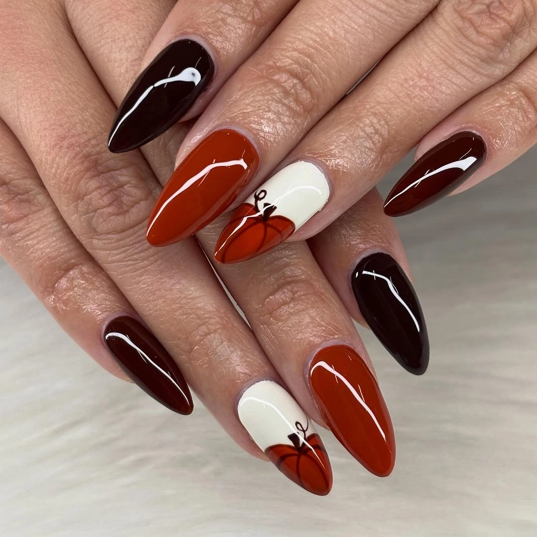 Long pointed burgundy black nails with orange pumpkin accents