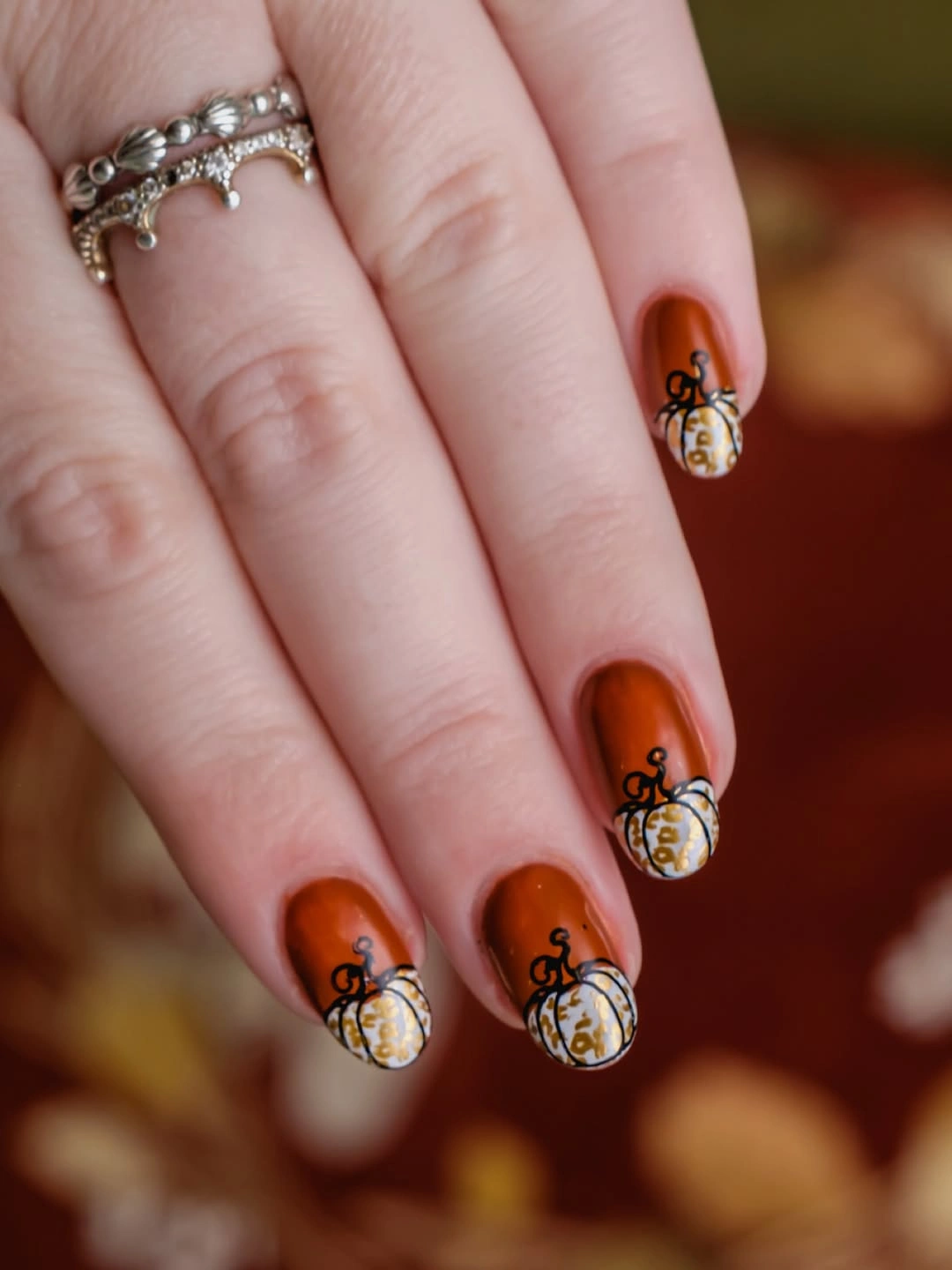 Short rounded pink nails with tiny orange pumpkin and leaf details