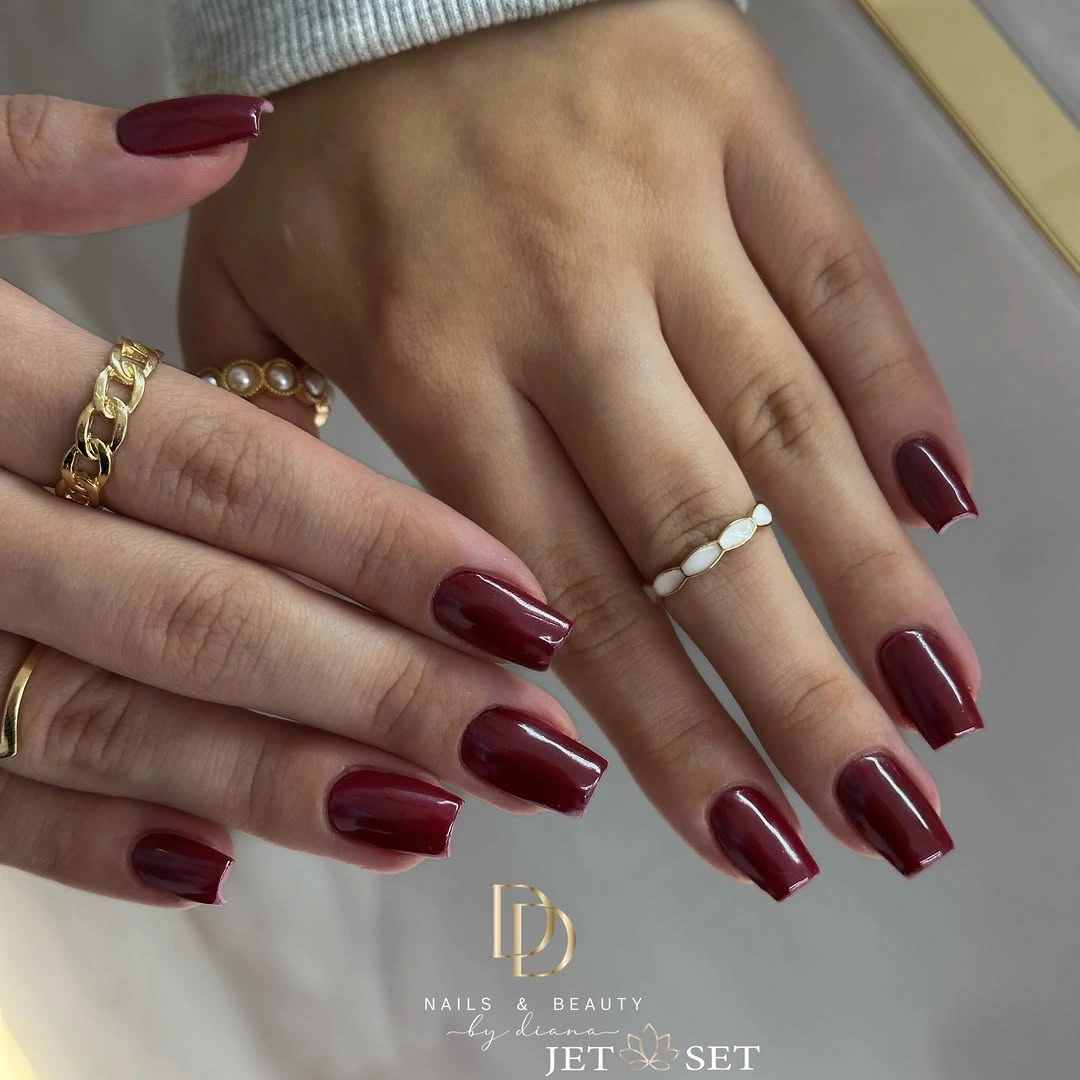 Glossy burgundy square nails with metallic jewelry nearby