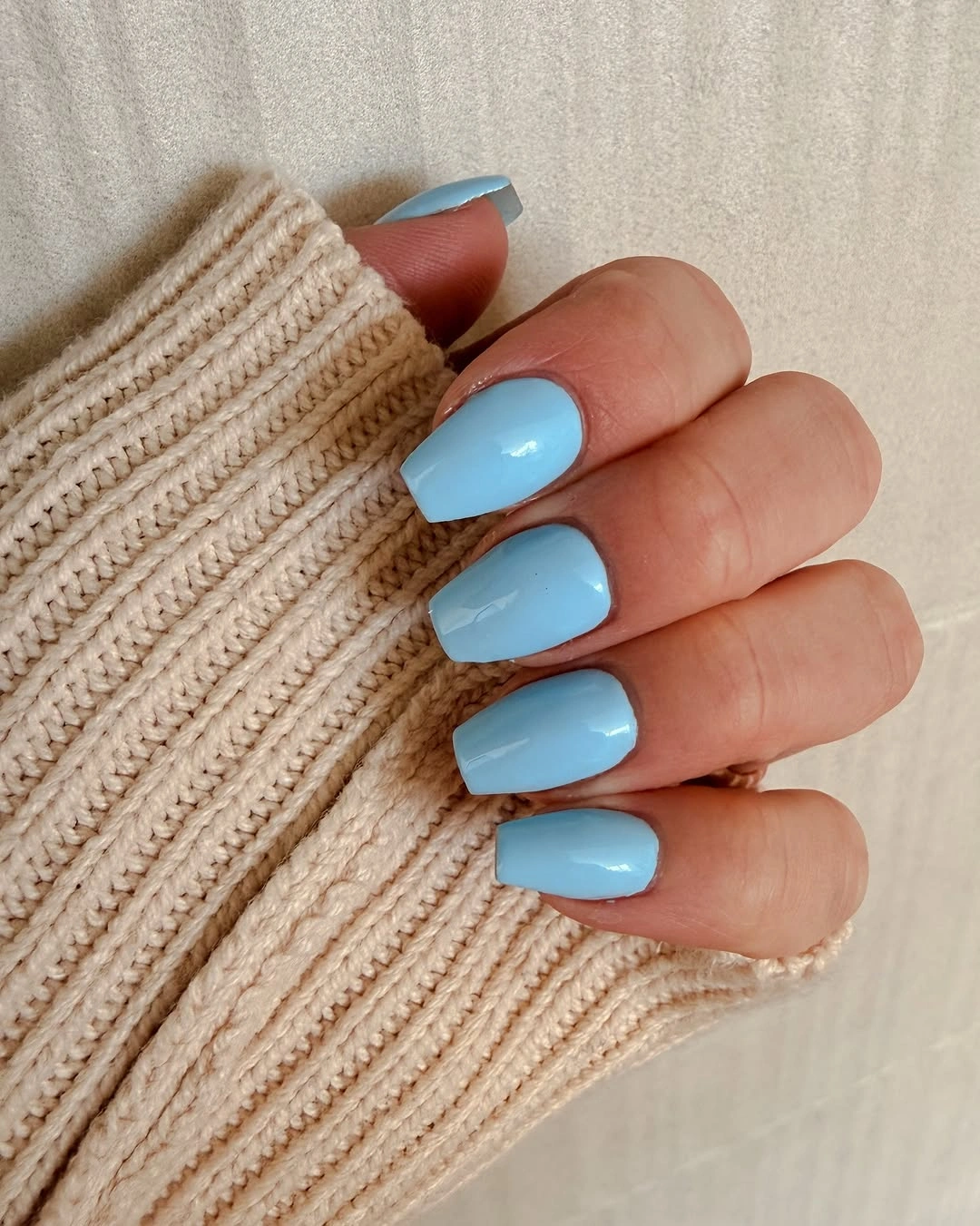 Pale blue short square nails against a beige knit sleeve