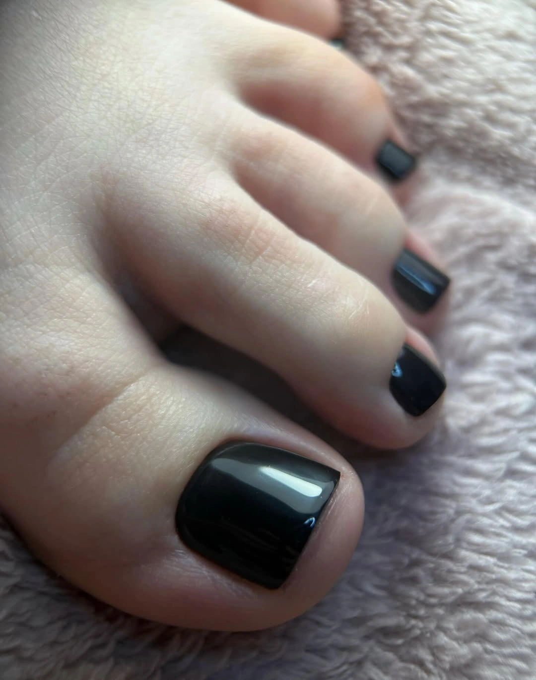 Glossy black short square toenails against soft ribbed fabric