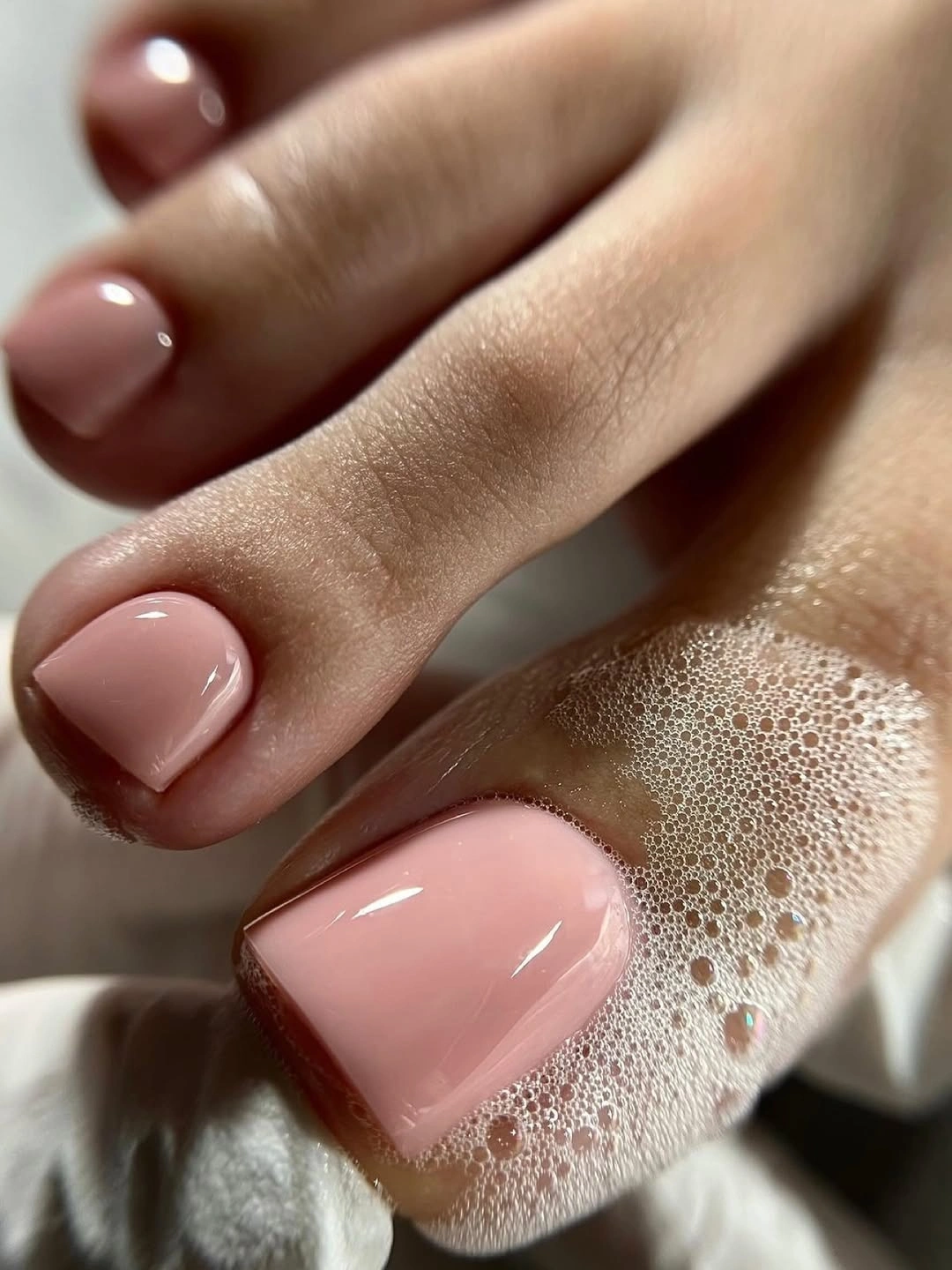 Soft blush pink glossy short square toenails near a towel