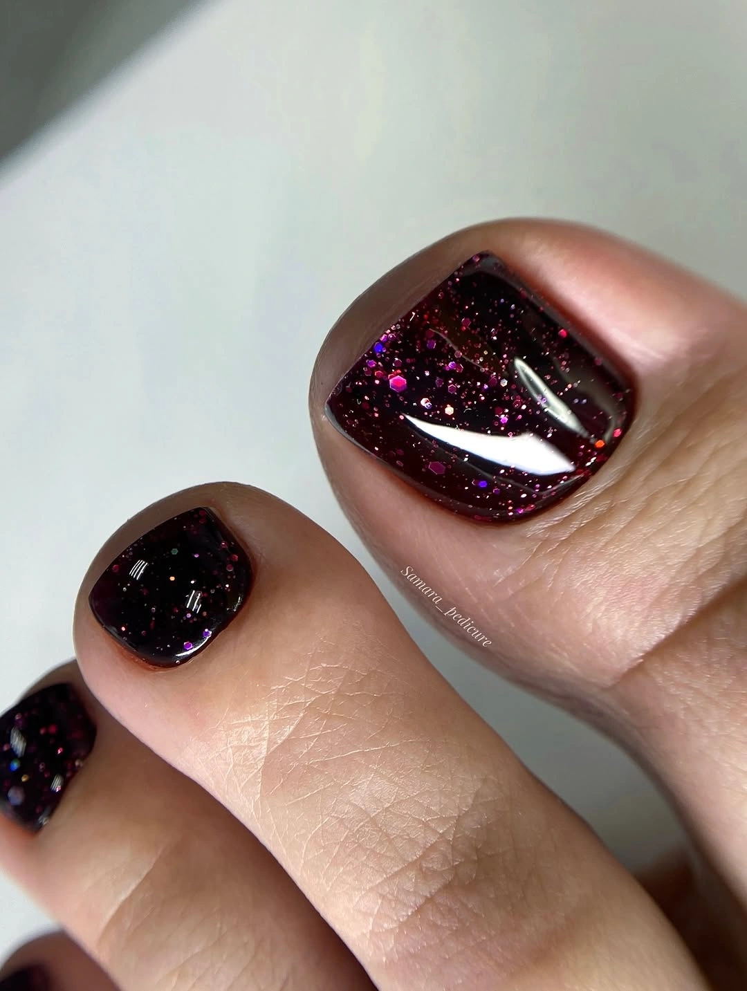 Deep burgundy glitter toenails with bright reflective sparkle