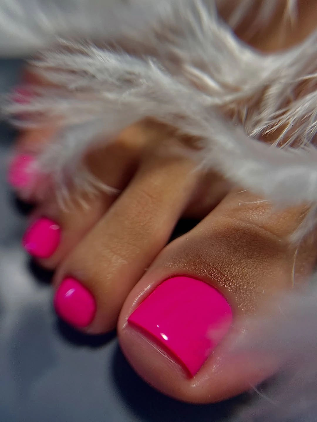 Glossy bright pink short square toenails beside pale feathers