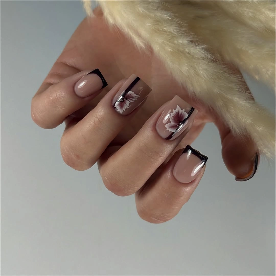 Short nude square nails with black edges and pale floral accents