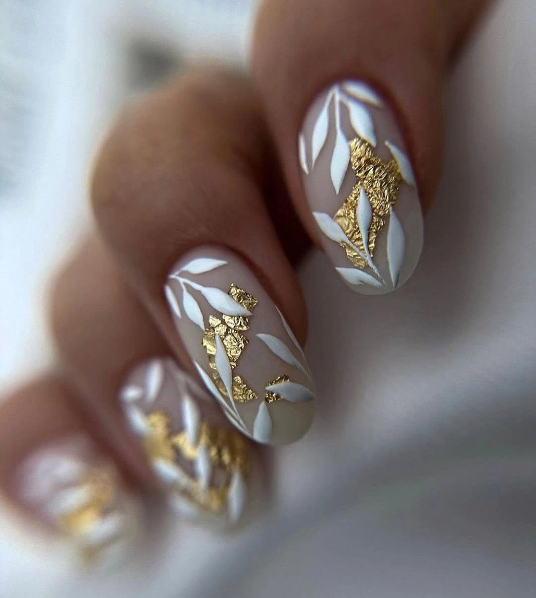 Neutral almond nails with white leafy art and gold accents