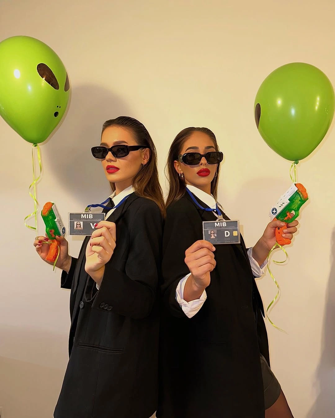 Two girls in black agent suits with sunglasses green alien headbands and balloons